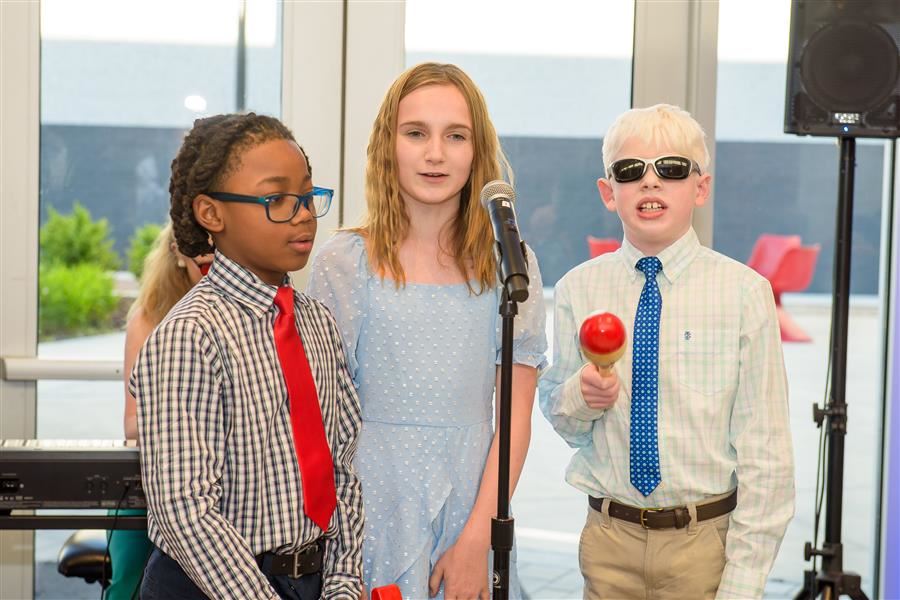 Three students singing into a microphone. One plays the maraca.